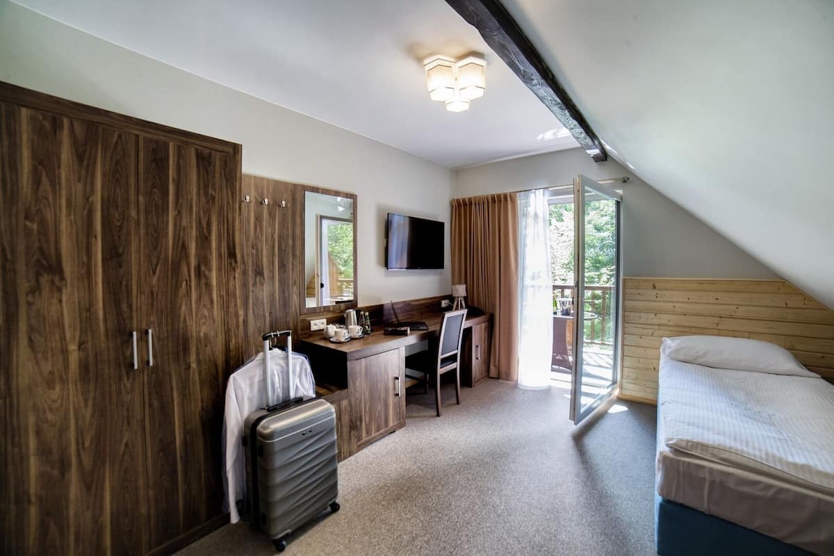 Une chambre avec un lit, un bureau, une chaise, une valise, une télévision et un balcon avec vue.