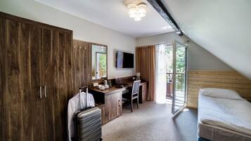 Un dormitorio con cama, escritorio, silla, maleta, televisión y balcón con vistas.