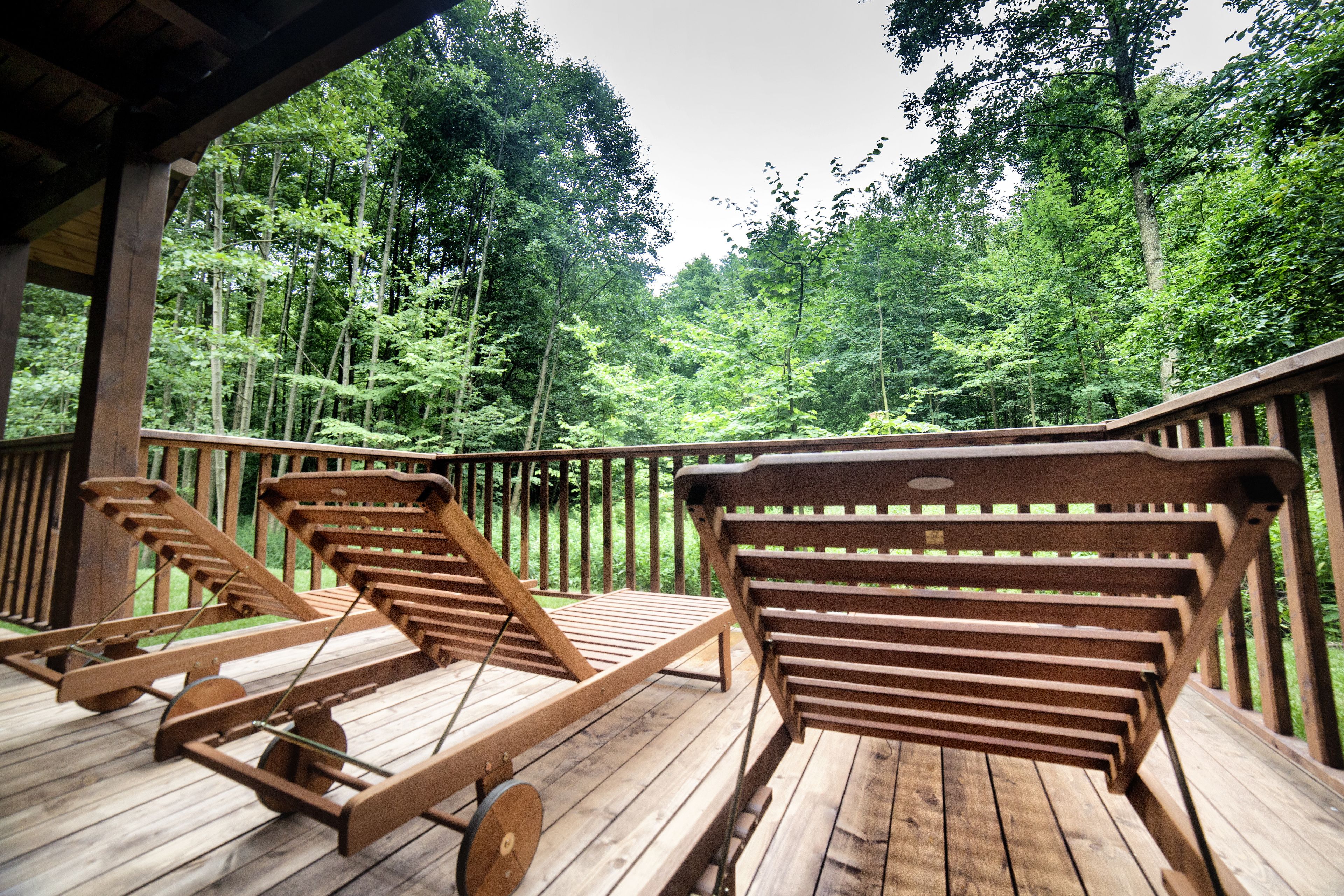 A wooden deck with two lounge chairs and a wooden railing, surrounded by a forested area.