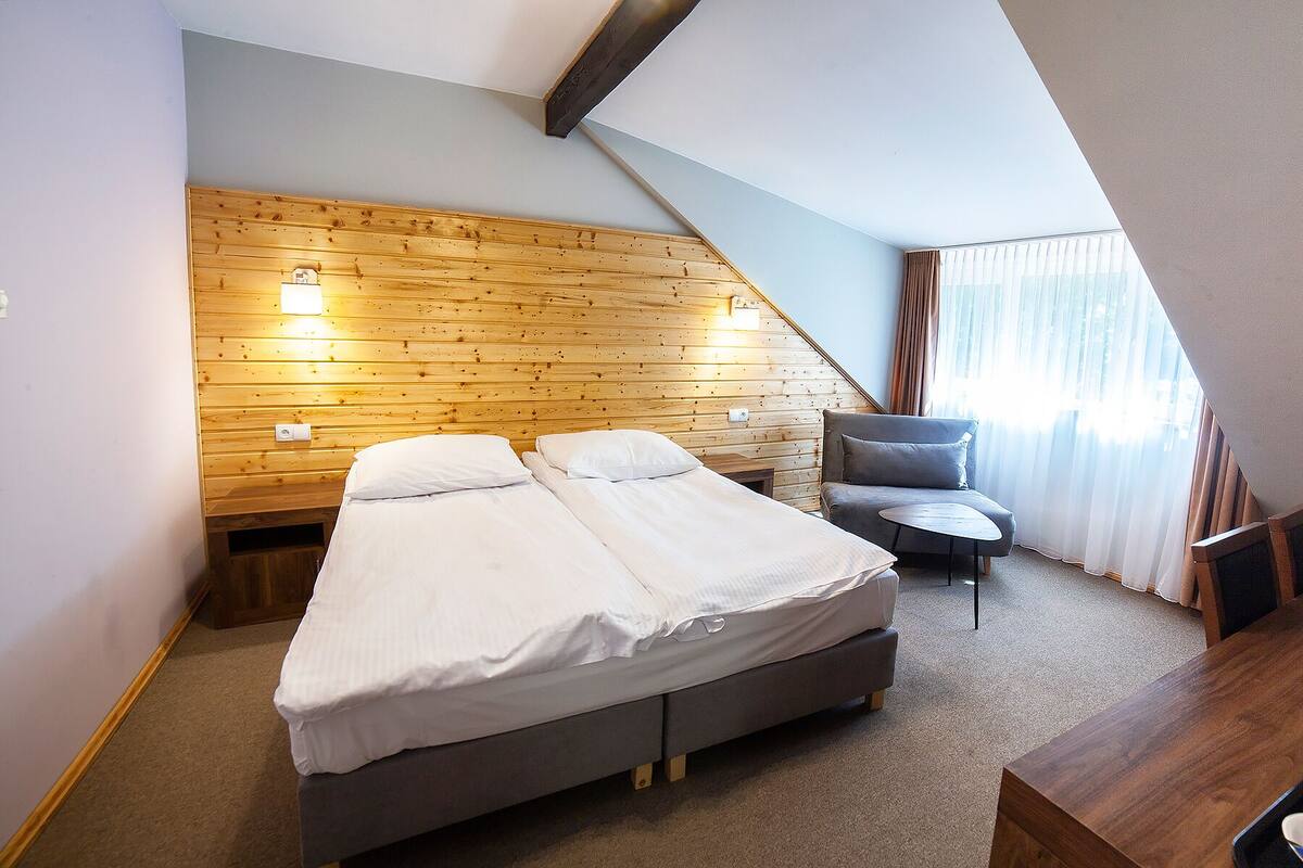 Une chambre avec un plafond en pente en bois, un lit, une chaise et une petite table.