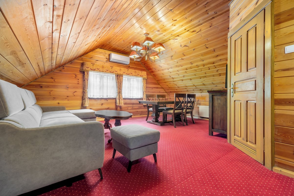 Une pièce mansardée chaleureuse avec un plafond en bois, un canapé, une table à manger avec des chaises et une moquette rouge.