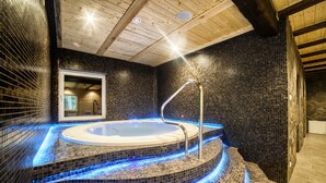 Un bain à remous doté d’un éclairage LED bleu, d’un plafond en bois et de murs recouverts de mosaïques.