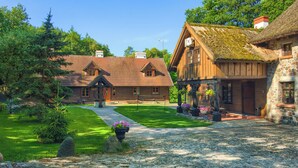 Un bâtiment traditionnel en bois, doté d’une façade en pierre, d’un toit de chaume et d’un jardin bien entretenu avec un chemin pavé.