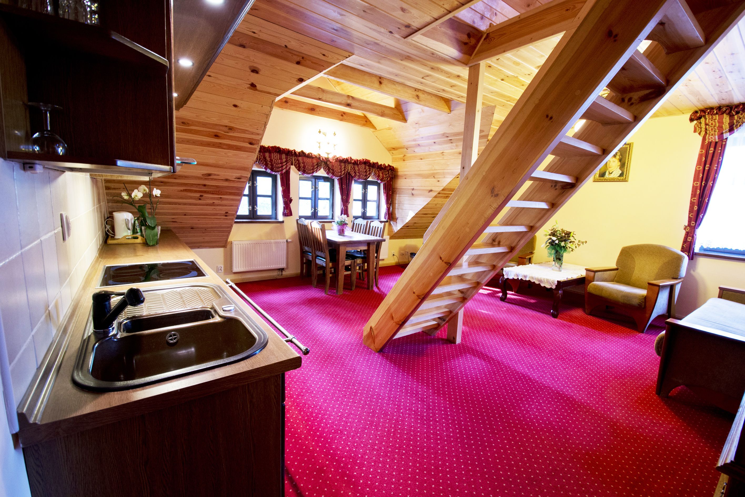 A cozy cabin with a kitchen, dining area, and a red carpeted floor.