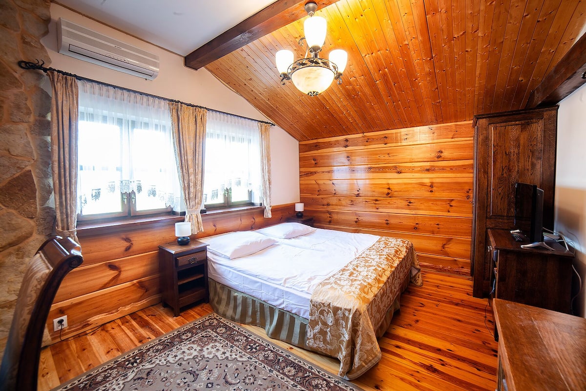 Une chambre à coucher aux murs lambrissés, comprenant un lit, des tables de chevet, un bureau et un ventilateur de plafond.