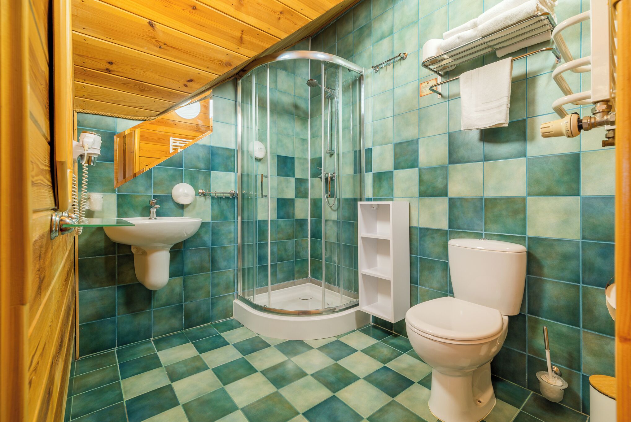 A bathroom with a glass-enclosed shower, a sink, a toilet, and a shelf.