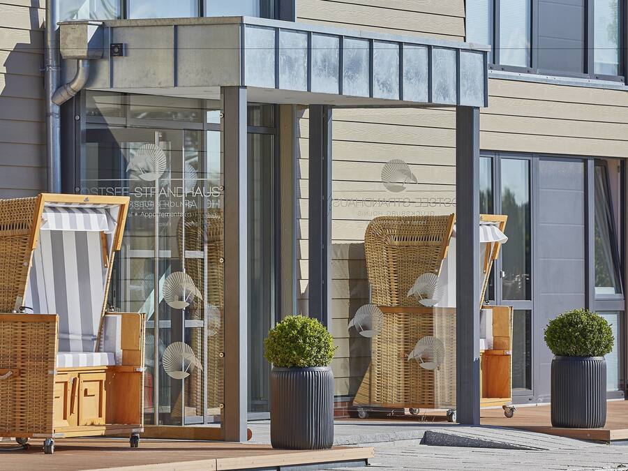 A modern building with a covered outdoor seating area featuring wicker furniture and potted plants.