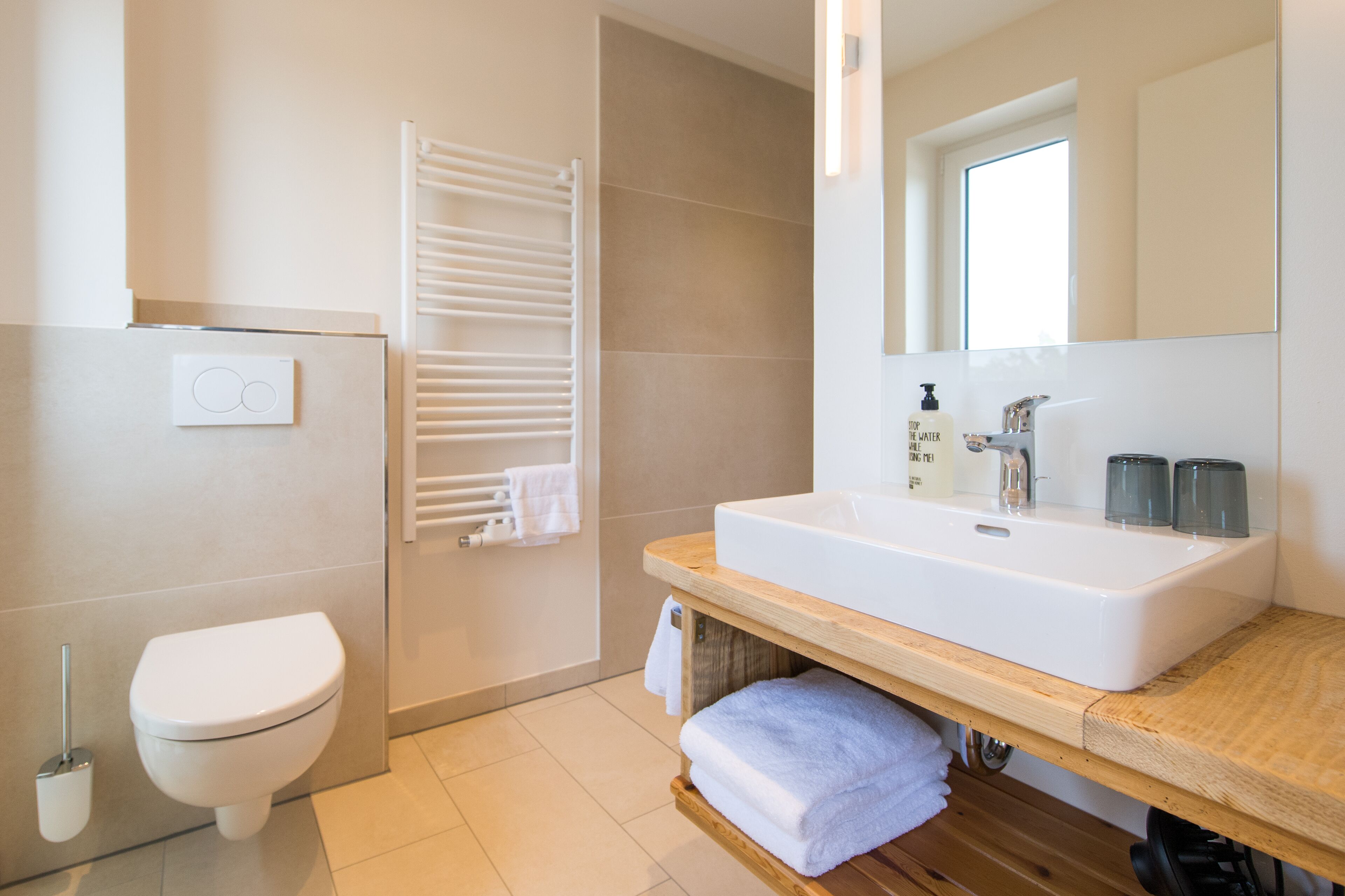 Une salle de bain moderne avec des toilettes blanches, un porte-serviettes, un meuble-lavabo en bois et un miroir.