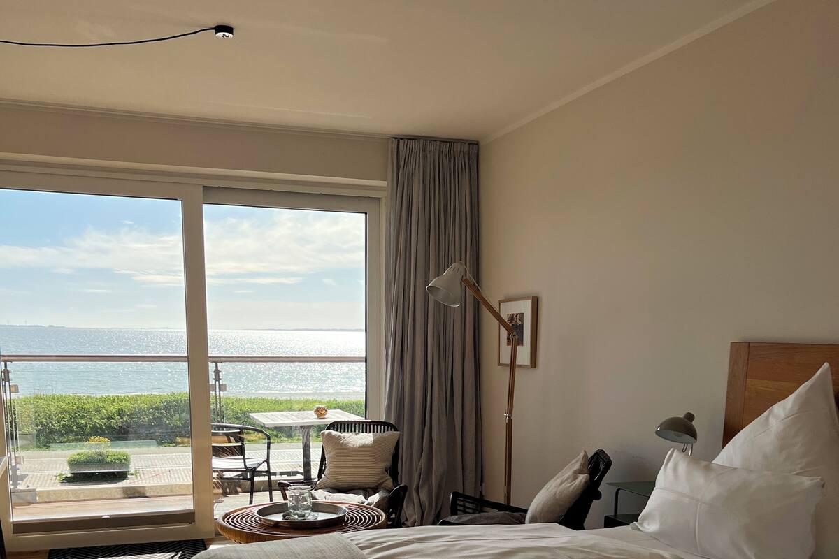 Een hotelkamer met een groot bed, een bureau, een stoel en uitzicht op zee.