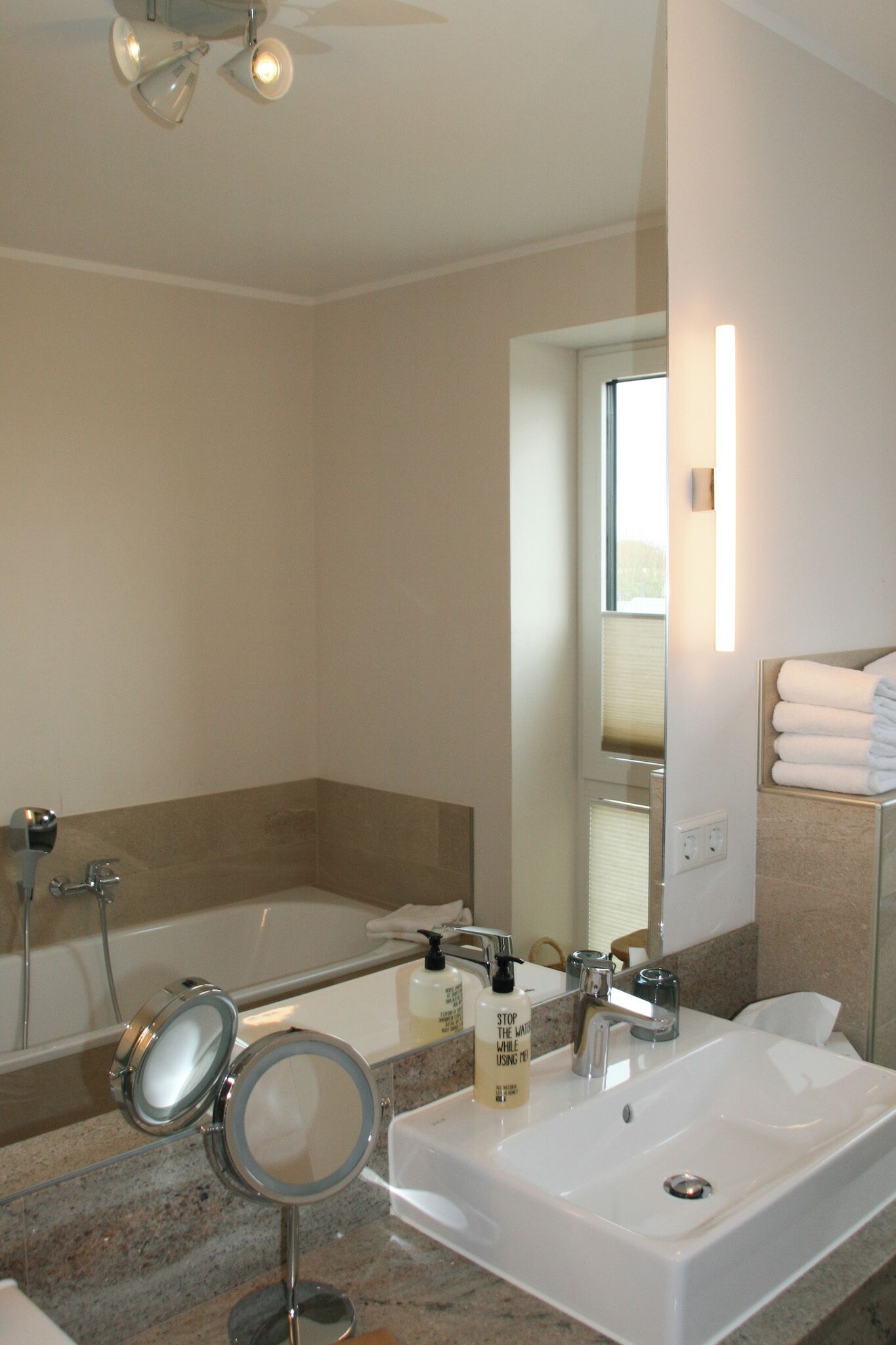 A modern bathroom with a large mirror, a sink, a shower, and a towel rack.