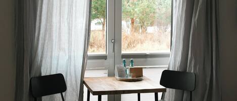A room with a table and two chairs, a window with curtains, and a view of trees outside.