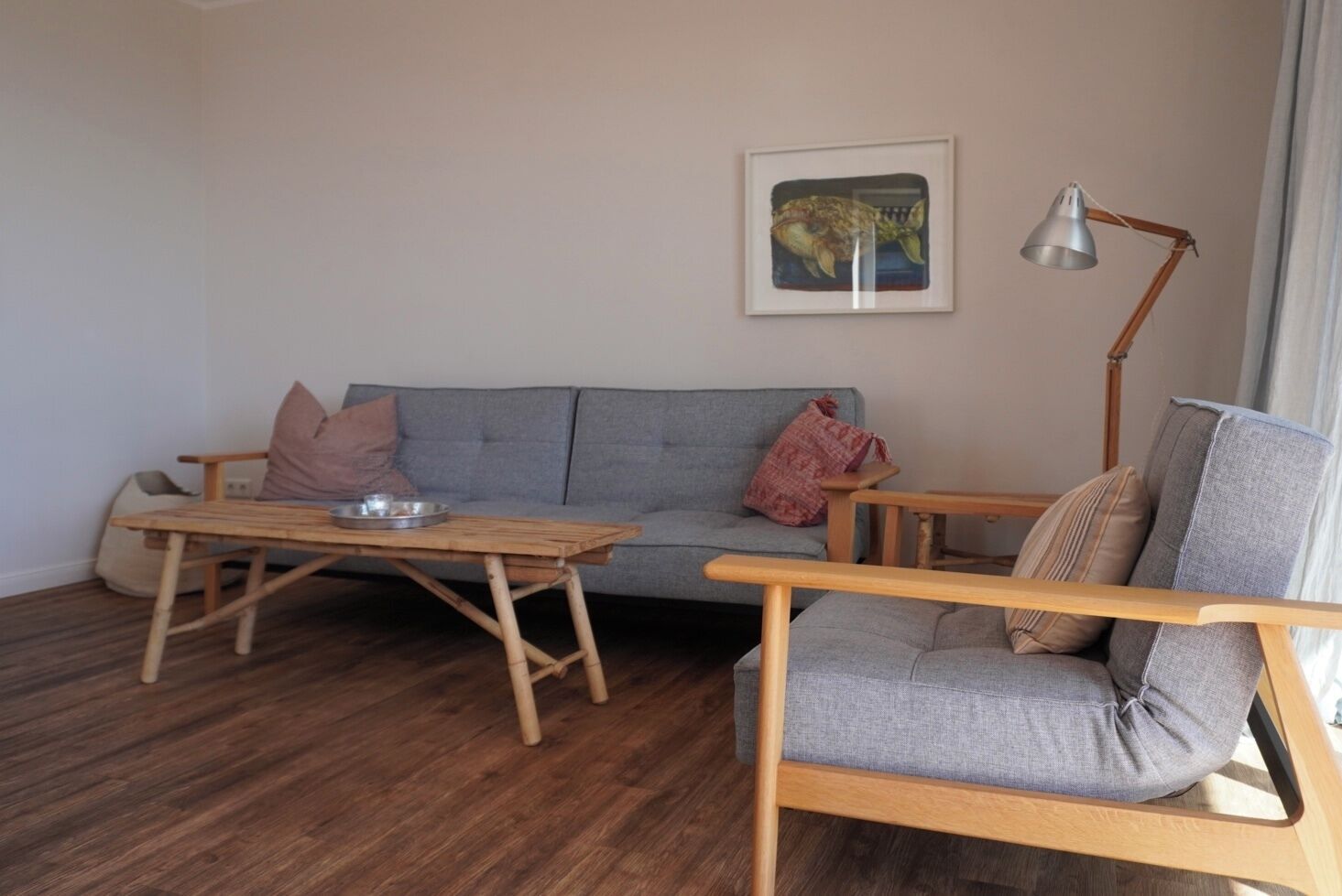 A living room with a grey sofa, a wooden coffee table, a wooden armchair, a floor lamp, and a framed picture on the wall.