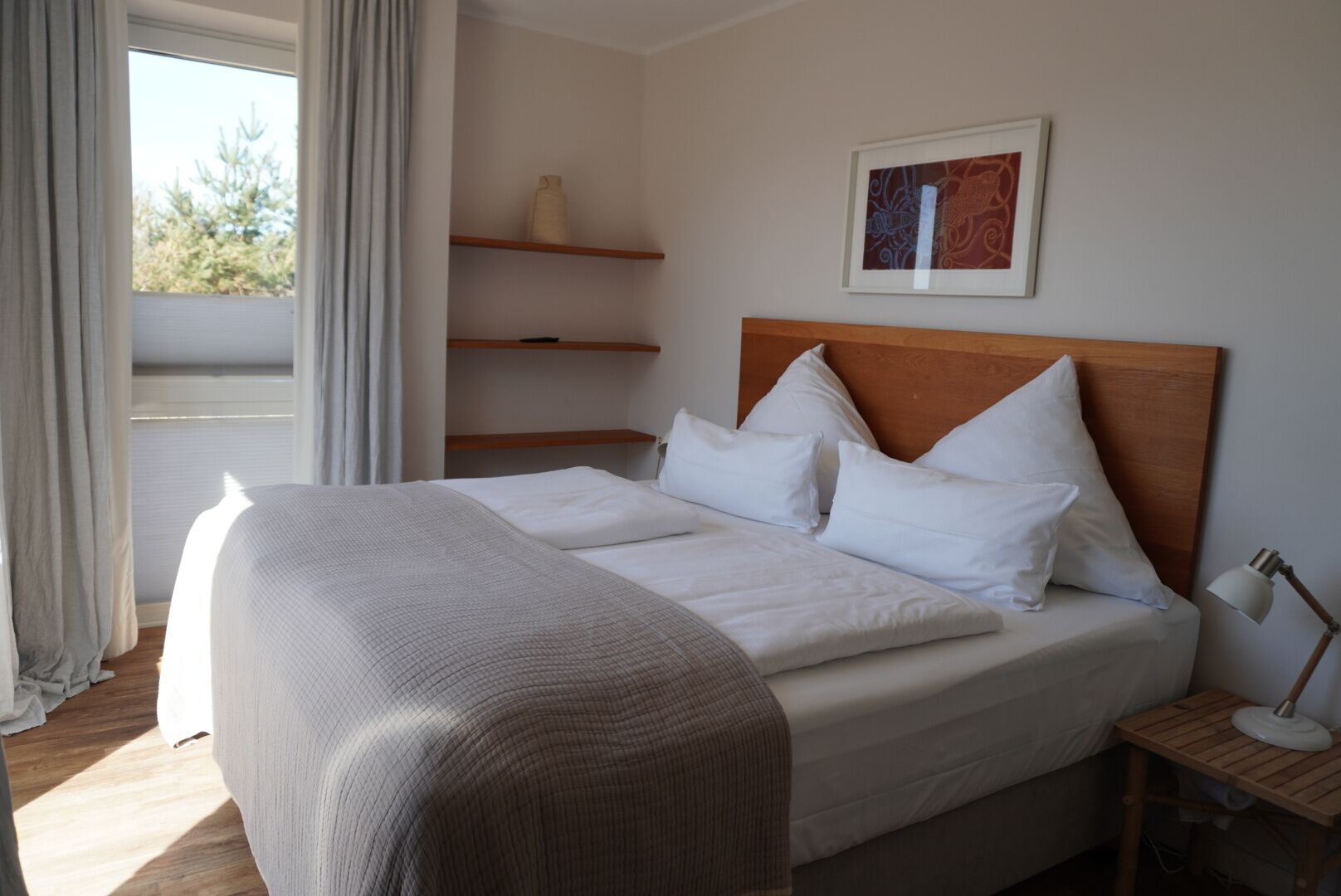 Una cama bien hecha con sábanas blancas, cabecera de madera y mesita de noche con lámpara.