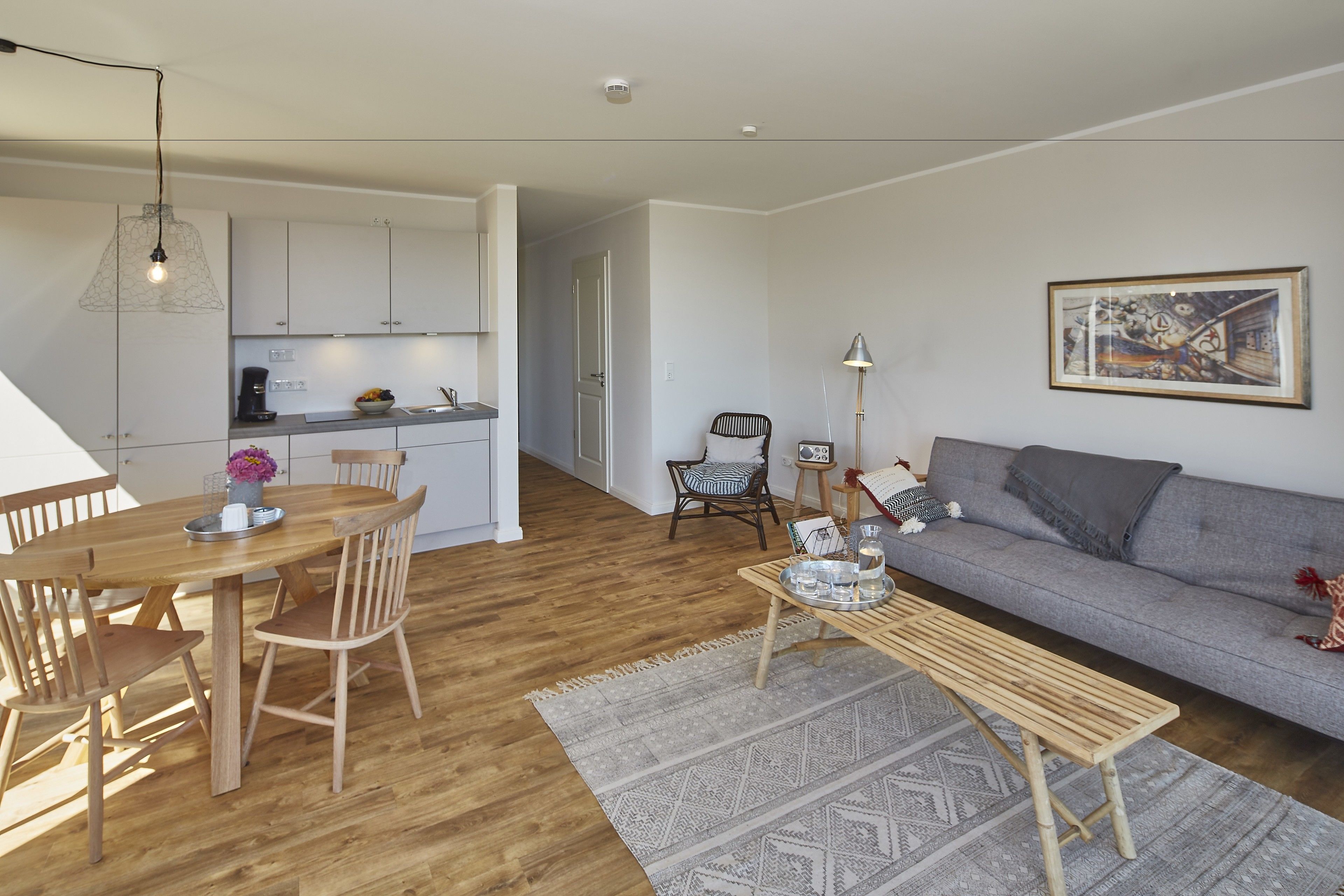 Un salon moderne avec une table à manger en bois, un canapé gris et une cuisine en arrière-plan.