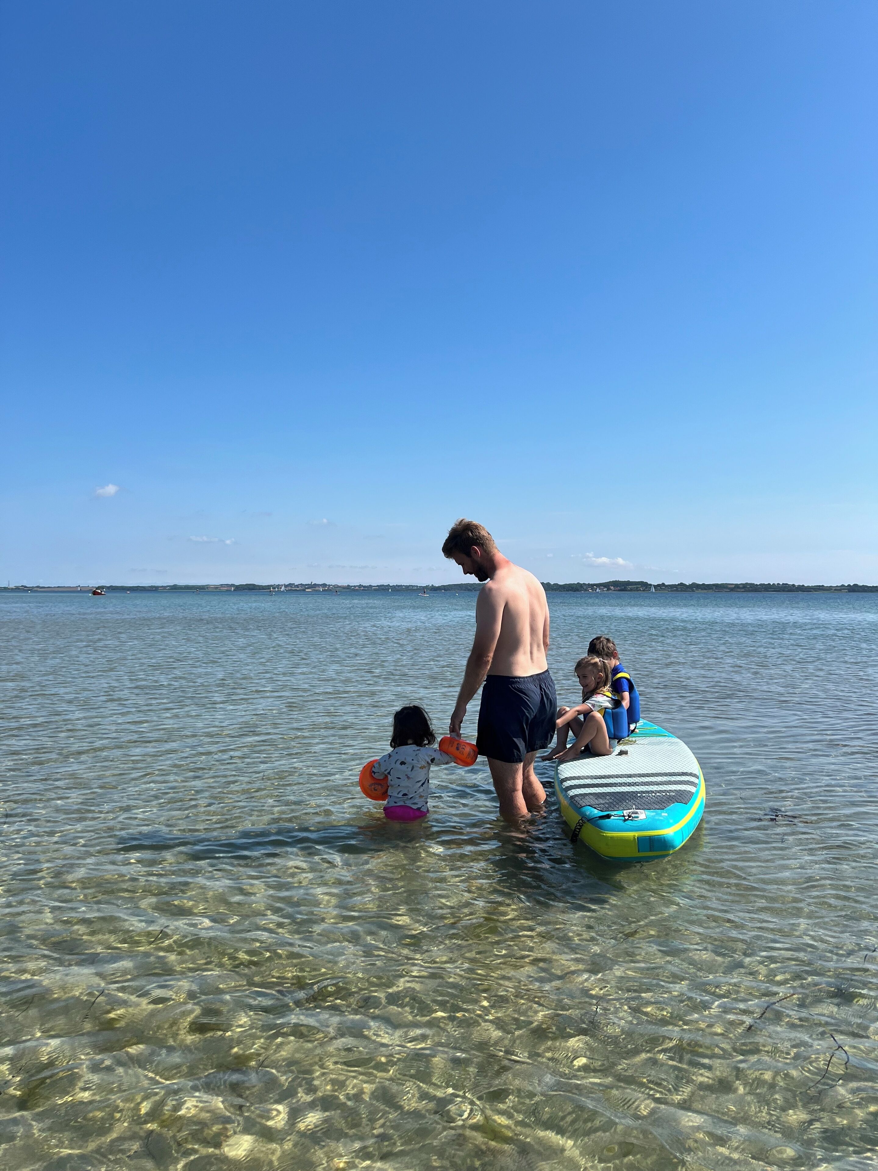 A man and two children in shallow water near a body of water, with a clear sky above.