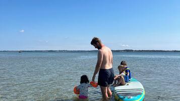 A man and two children in shallow water near a body of water, with a clear sky above.