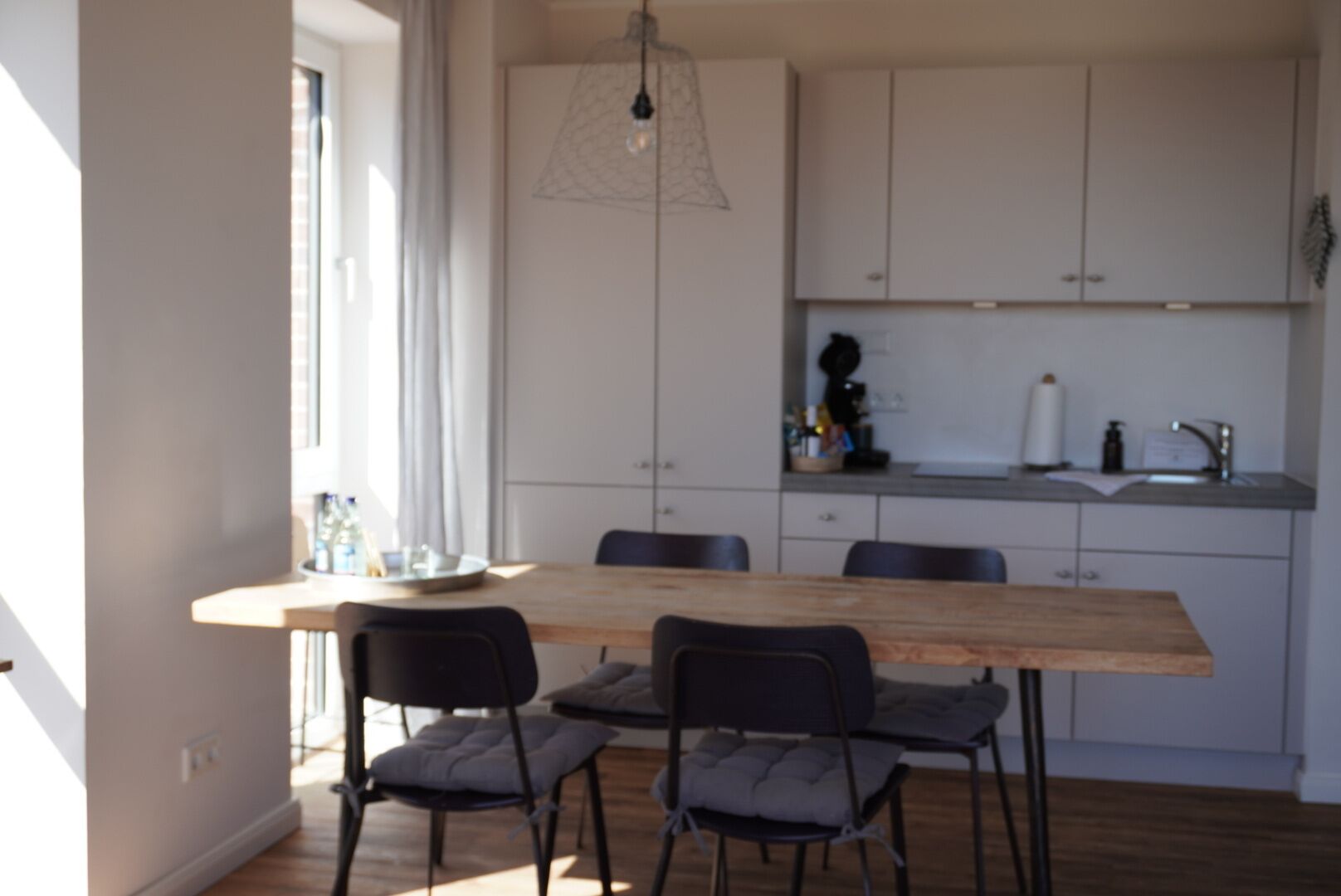 Moderni keittiö, jossa on puinen ruokapöytä, mustat tuolit ja valkoiset kaapit.