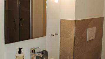Een badkamer met een wit wastafel, een spiegel, een douche en een toilet.