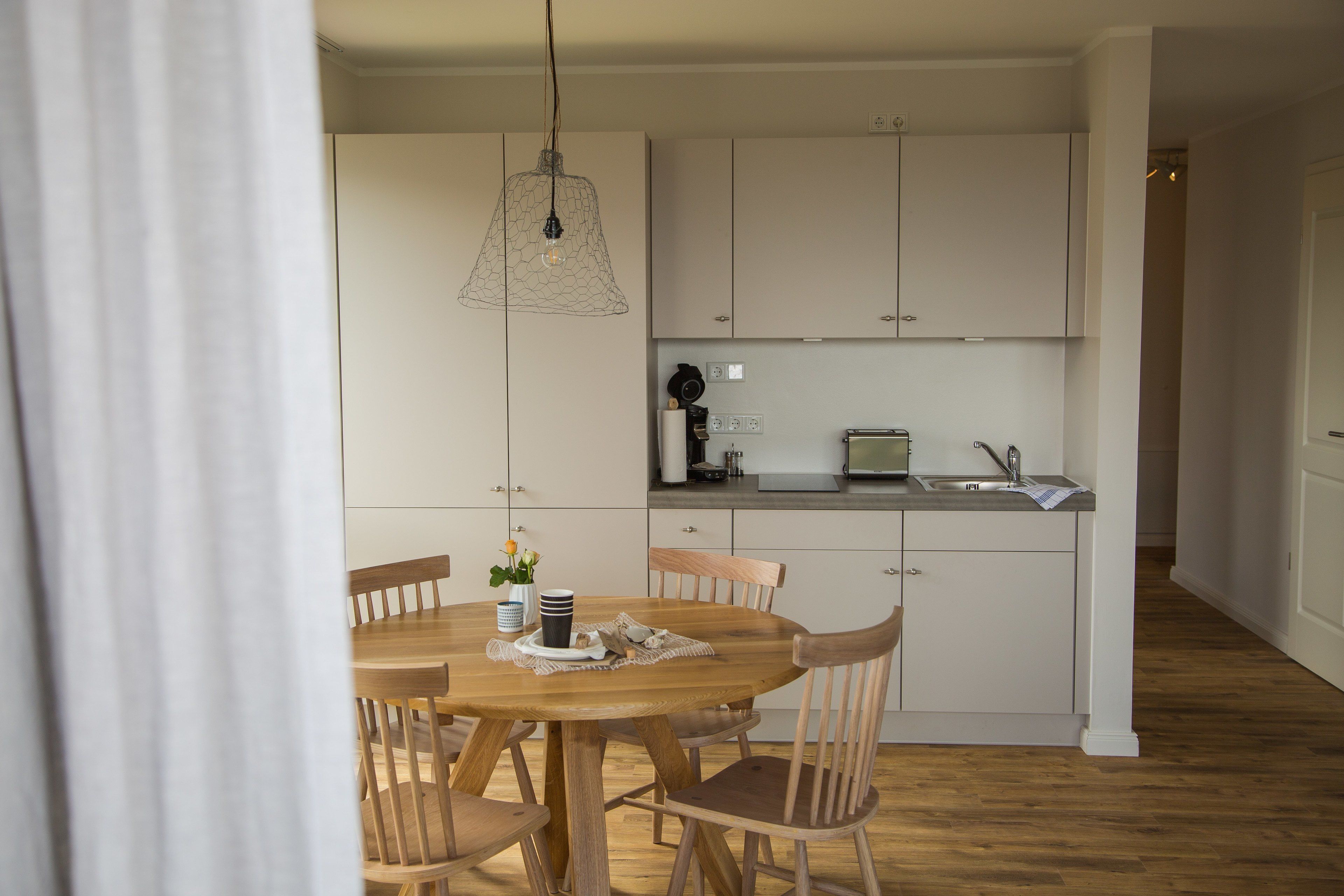 Una cocina moderna con armarios blancos, una mesa de comedor de madera y una lámpara colgante.