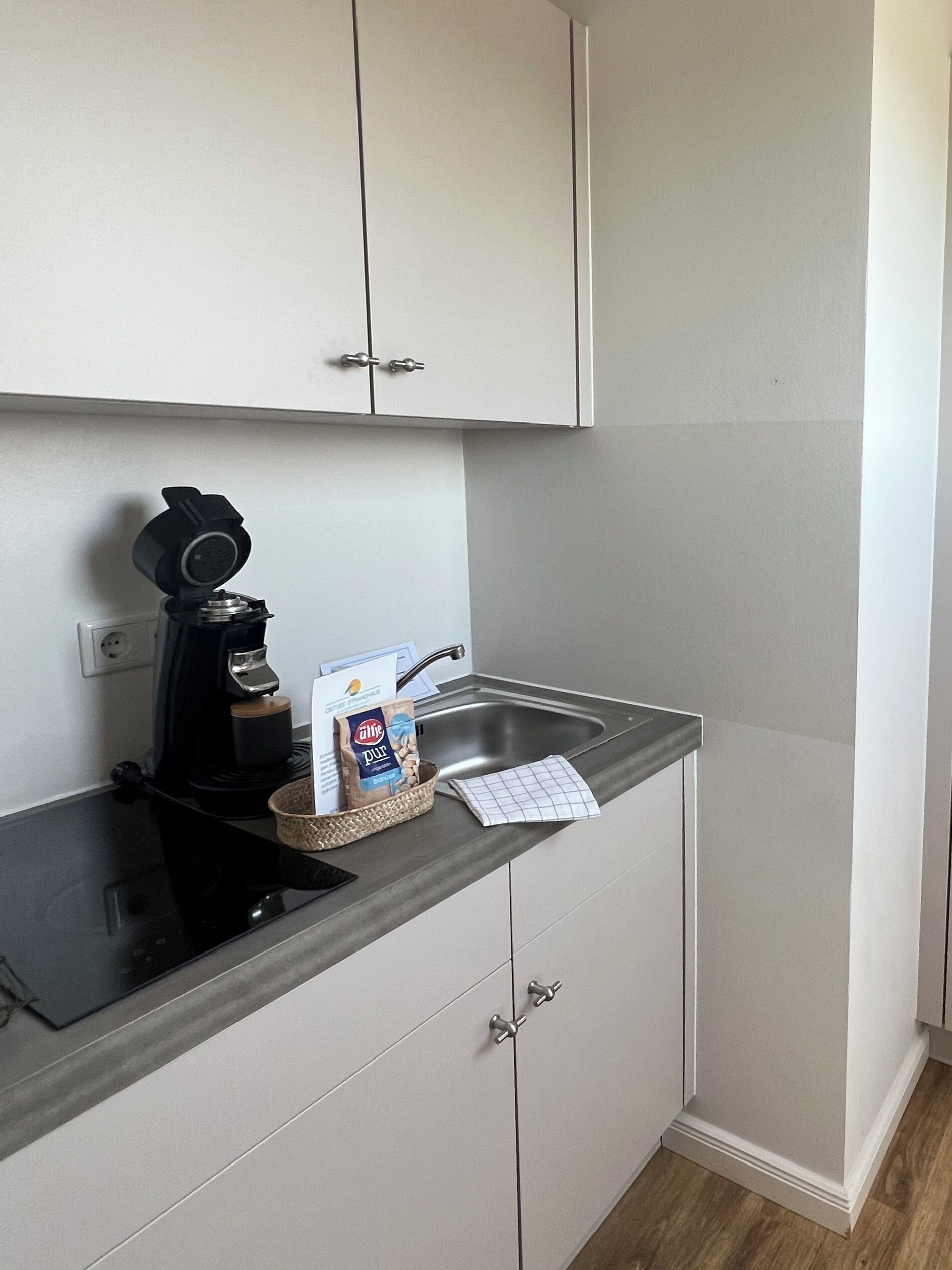 A small kitchenette with a coffee maker, a basket with a bag of coffee, a sink, and a countertop.