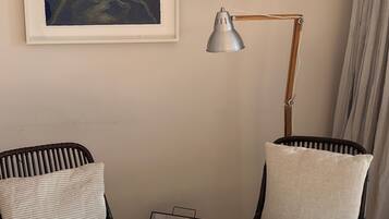 A room with two wicker chairs, a framed artwork, a floor lamp, and a tray with decorative items.
