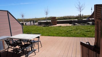 Een houten terras met een tafel en stoelen, een bakstenen muur en een gazon met bomen.