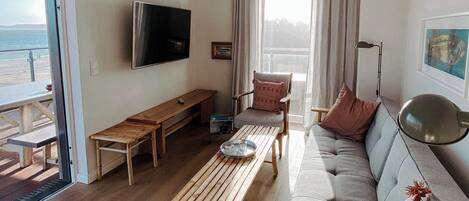 Una sala de estar con sofá, mesa de centro de madera, televisor y una silla.