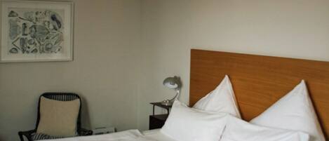 A hotel room with a bed, a chair, a bedside table, and a ceiling light.