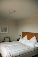 Una habitación de hotel con una cama, una silla, una mesita de noche y una lámpara en el techo.