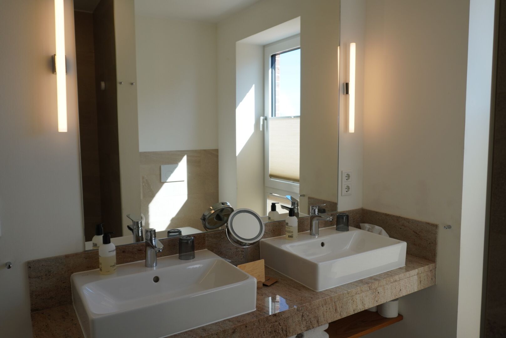 Un baño con dos lavamanos, un espejo grande y una ventana.