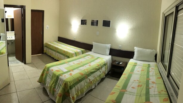 A hotel room with two single beds, a small bedside table, a mirror, and a window with blinds. - Pousada Porto Canal (Cabo Frio)