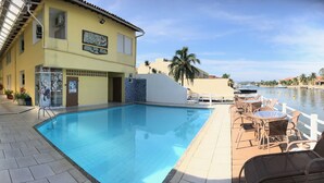 A swimming pool area with a building labeled "Pousada Porto Canal" and a view of the water. - Pousada Porto Canal (Cabo Frio)