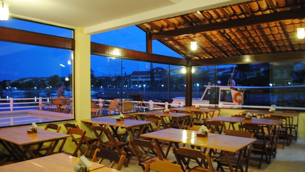 An indoor dining area with wooden tables and chairs, large windows, and a view of the outside. - Pousada Porto Canal (Cabo Frio)