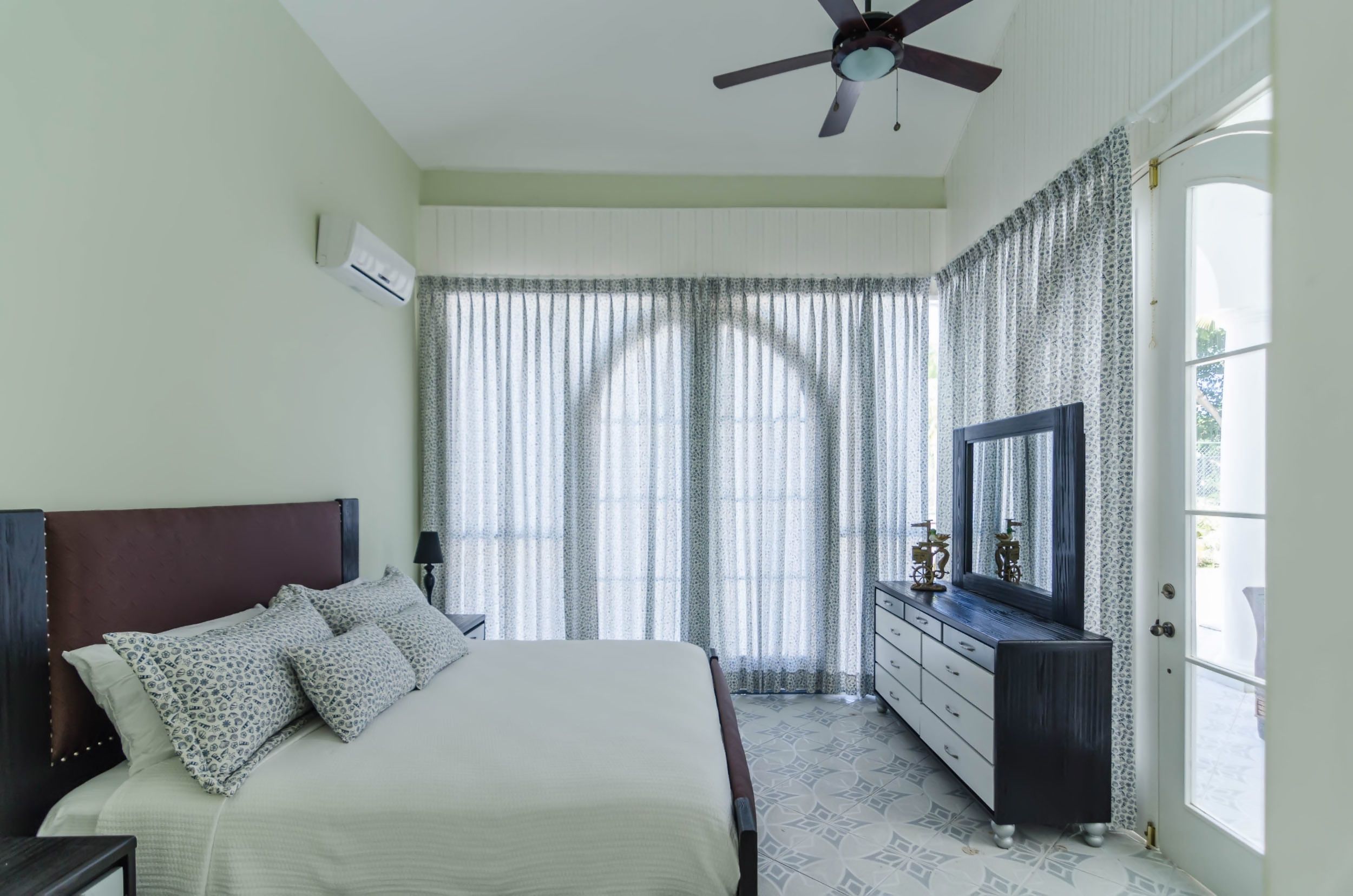 A bedroom with a bed, a dresser, a mirror, and a ceiling fan.