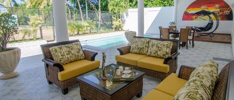 A sunlit patio with wicker furniture, a pool, and a tropical mural.