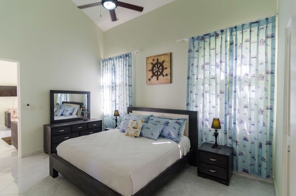 A bedroom with a bed, nightstands, a mirror, curtains, and a ceiling fan.