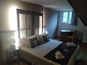 Quarto com cama, mesas de cabeceira, escrivaninha e uma cadeira.