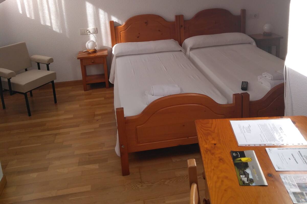 A bedroom with a wooden bed, a desk, and a chair. There is a window providing natural light.