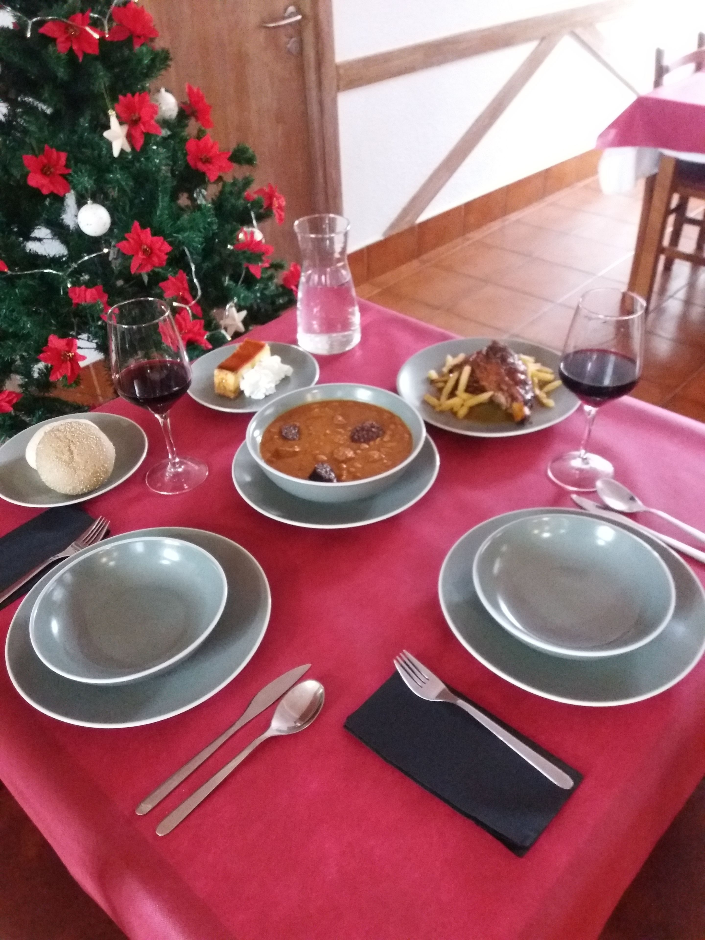A dining table set with plates, glasses, cutlery, and a Christmas tree in the background.