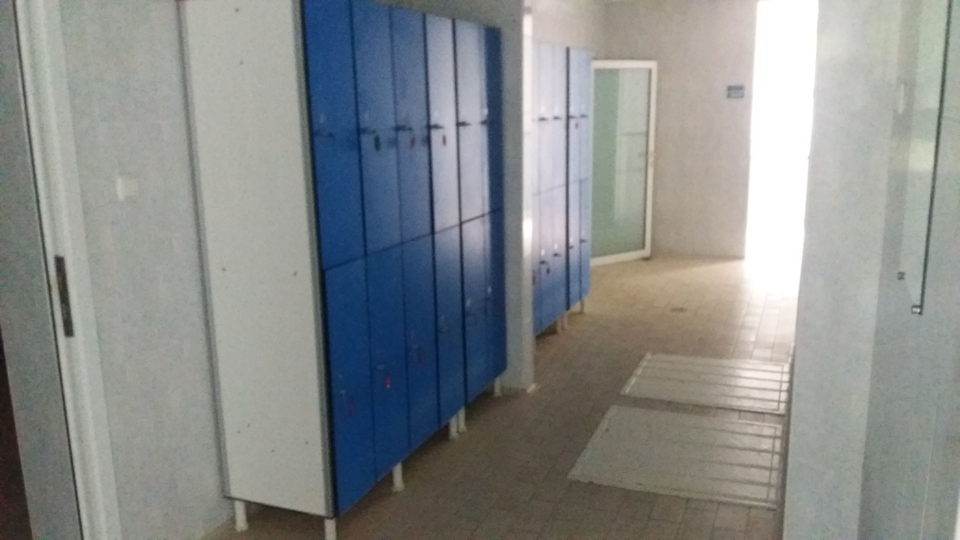 Un pasillo con taquillas azules y una puerta blanca.