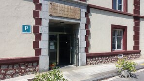 Um edifício com placa indicando sua fundação em 1871, sinal de estacionamento e uma parede de pedra com planta em vaso.