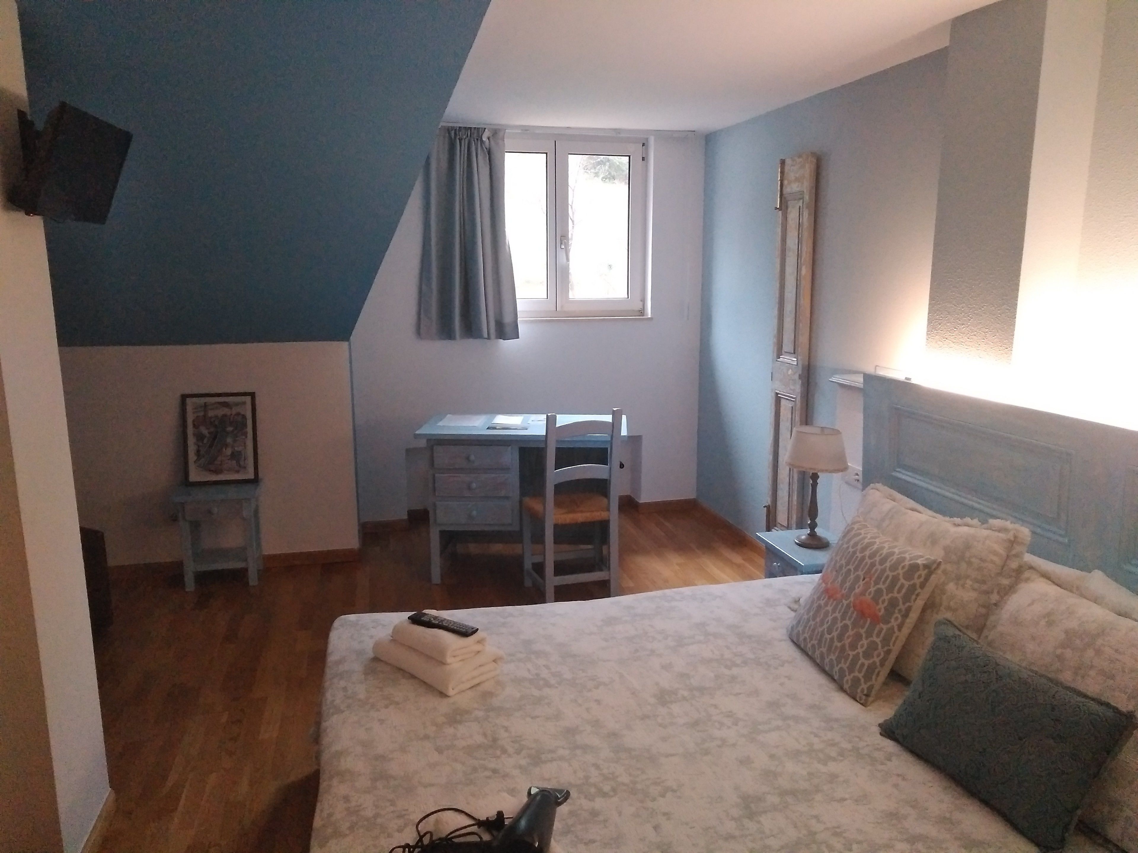 Une chambre à coucher avec un lit, un bureau, une chaise, une lampe et une fenêtre.