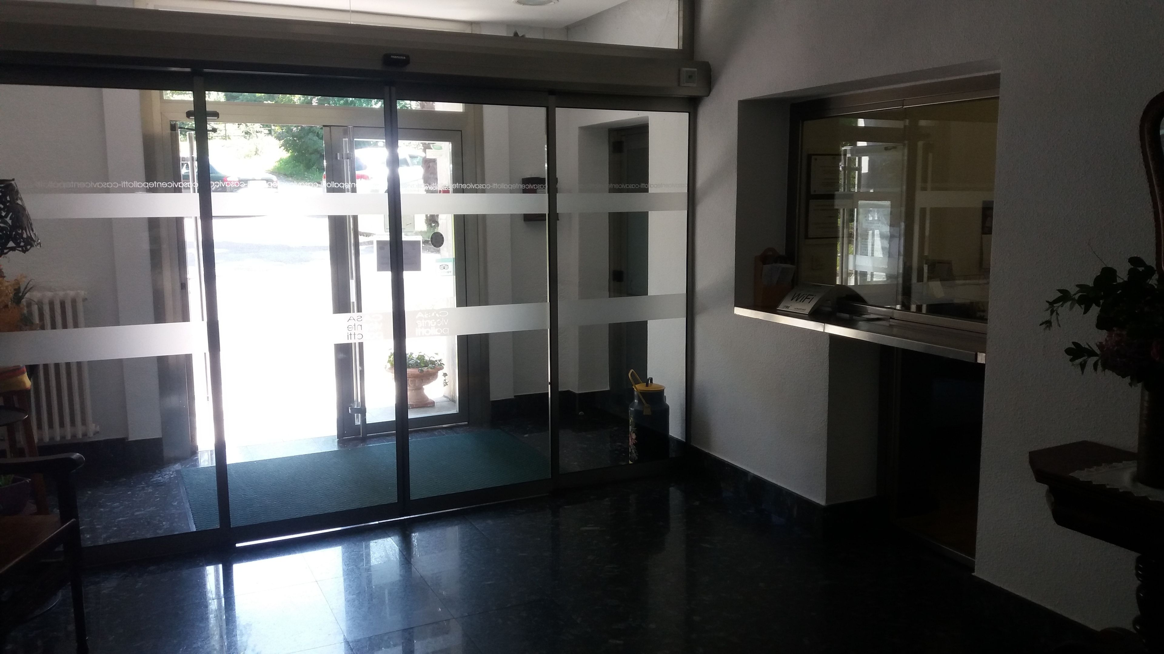 A hotel lobby with a glass door entrance, a reception desk, and a potted plant.