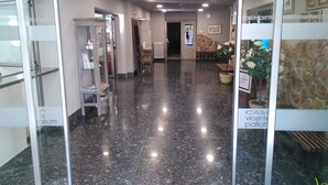 A hallway with a polished marble floor, glass doors, and a stone wall with a clock. - Balneario Casa Pallotti (Valle de Carranza)