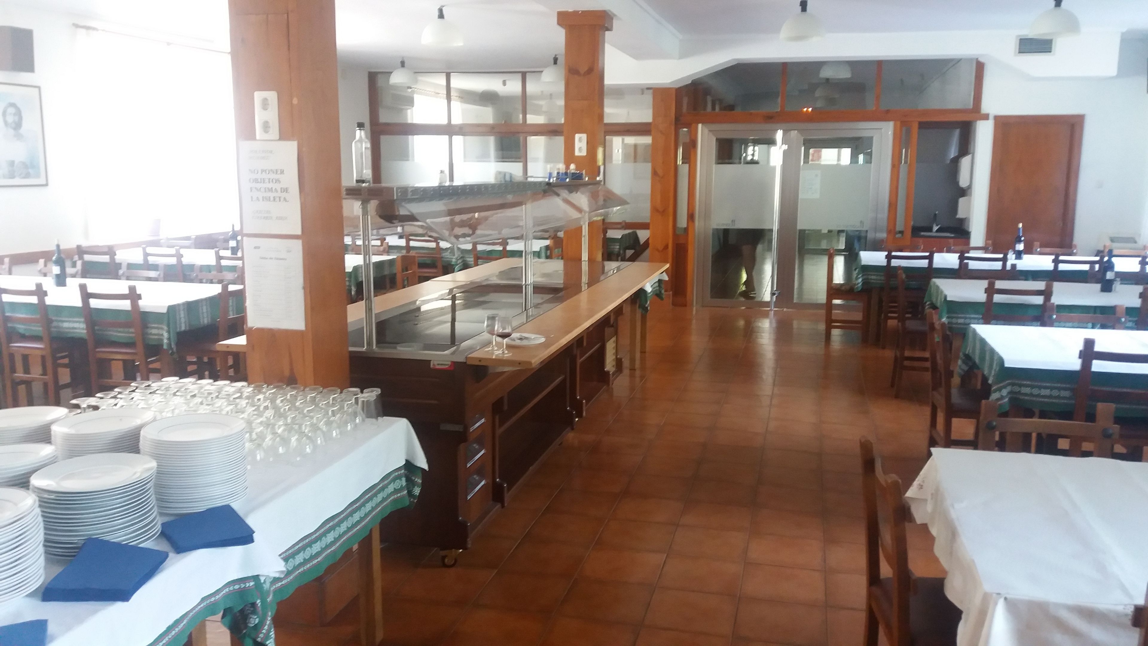 Un comedor con varias mesas, una barra de buffet y piso de baldosas.