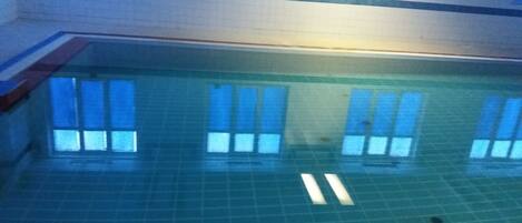 Una piscina interior con paredes de azulejos y ventanas que reflejan la luz.