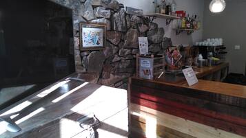 A bar area with a stone wall, wooden counter, and various bottles and cups.