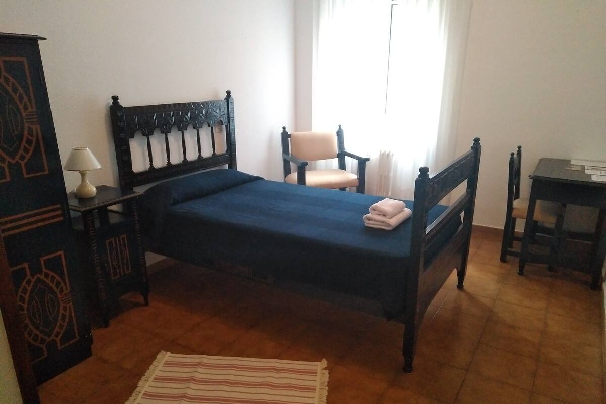 A room with a bed, a chair, a table, and a lamp.