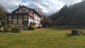 A large, multi-story building with a traditional architectural style, surrounded by a grassy field and trees. - Balneario Casa Pallotti (Valle de Carranza)