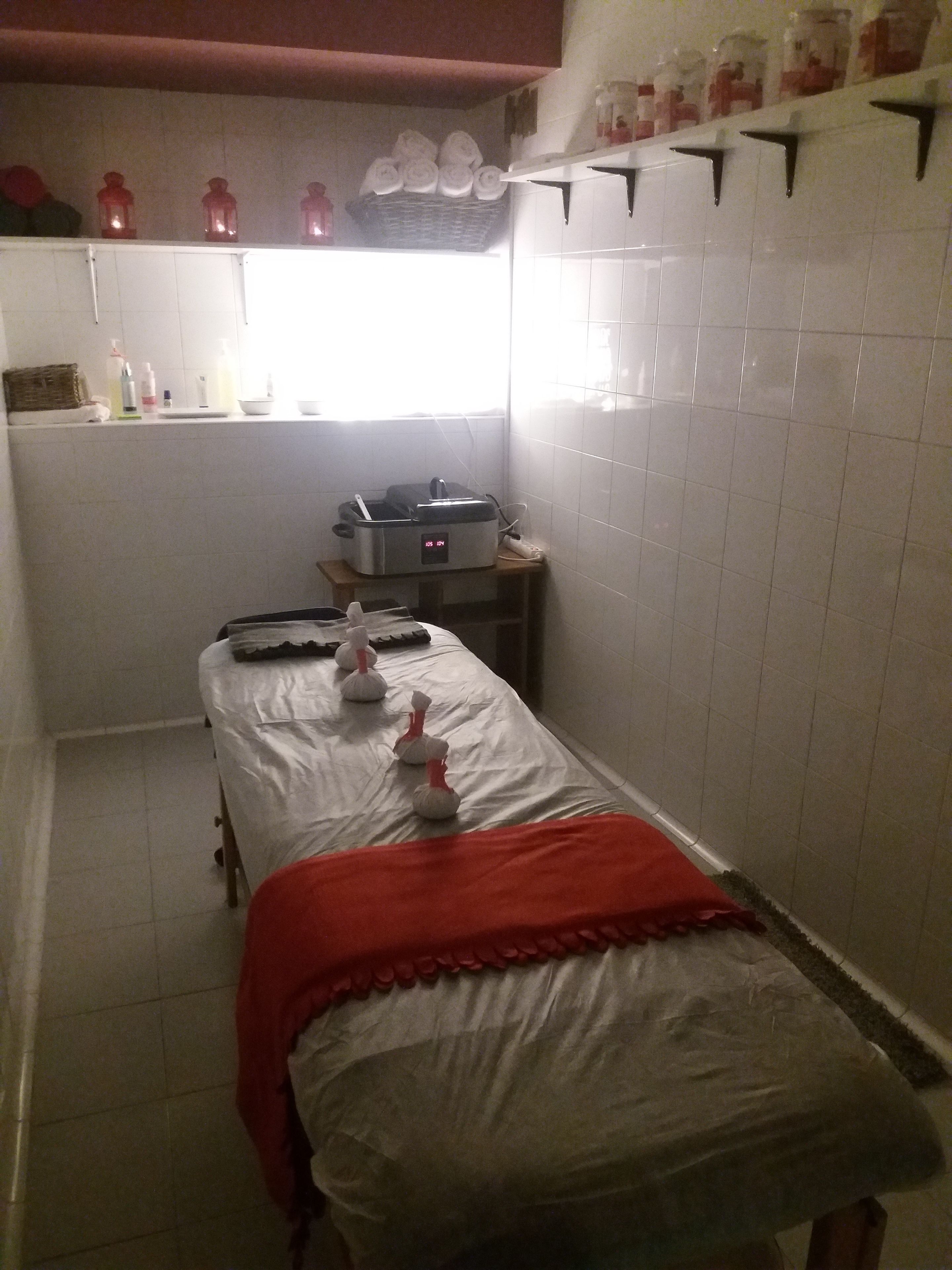 A small, narrow room with a bed, a small table with a heater, and a window with curtains.